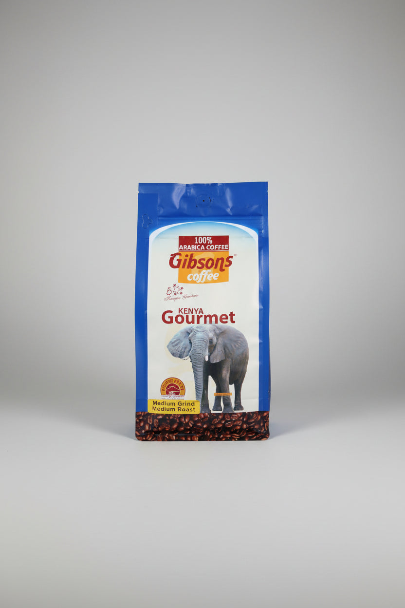 A bag of Gibson's Coffee Kenya Gourmet medium roast coffee, featuring a white and blue package with an elephant graphic and coffee beans at the bottom, set against a dark fabric background.