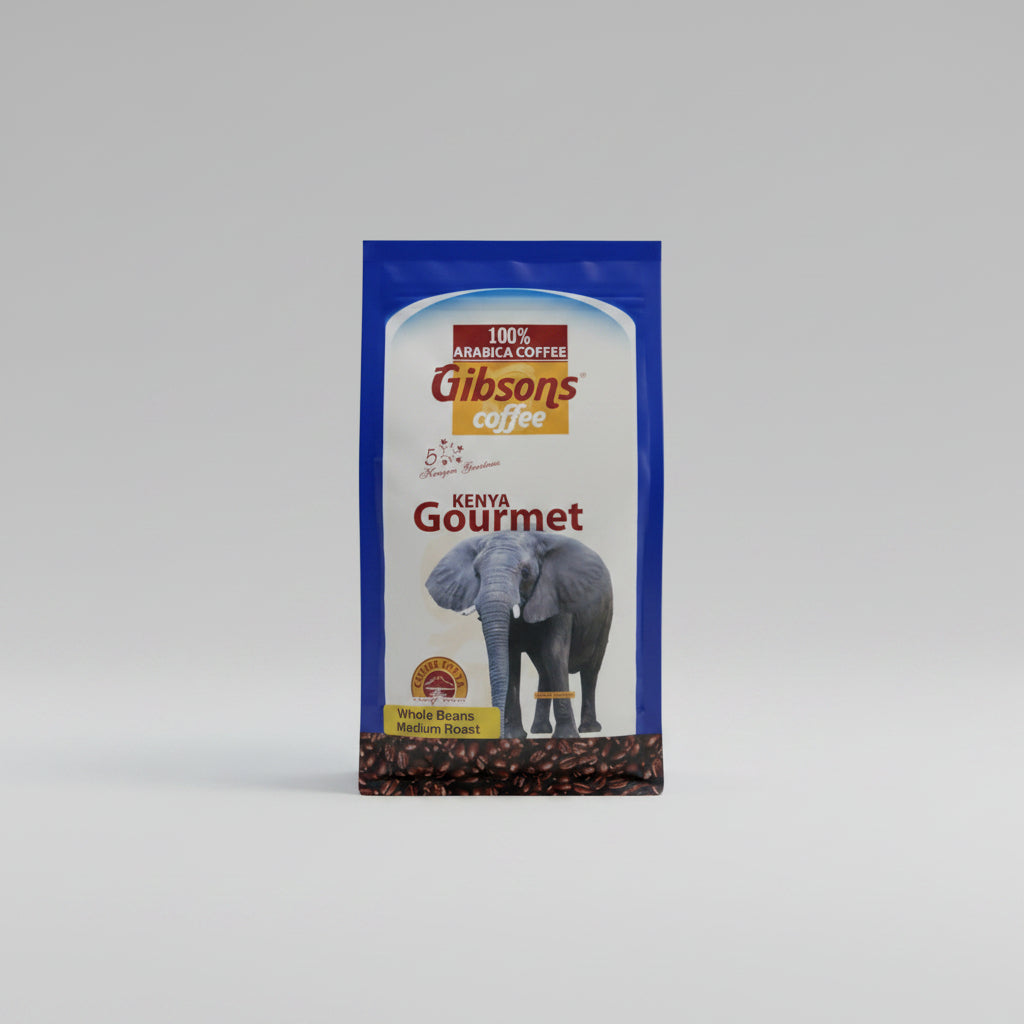 A bag of Gibson's Coffee Kenya Gourmet whole bean coffee sits on a dark navy blue fabric background. The packaging features a white and blue design with an illustration of an elephant and a visible layer of coffee beans at the bottom. Gibsons Kenyan whole bean coffee 400g, medium roast specialty coffee with rich aroma, smooth finish, and distinctive fruity character for coffee lovers who grind beans fresh before brewing.