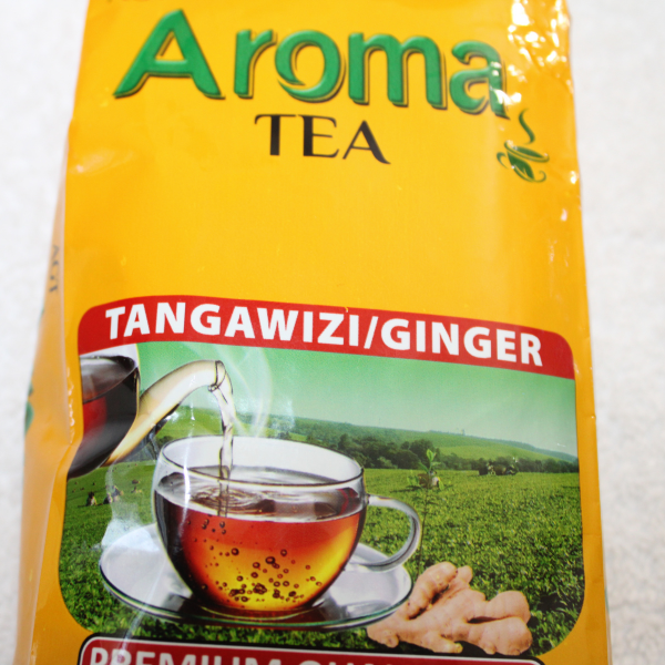 Close-up of Aroma Tea yellow bag front showing "Tangawizi/Ginger" red banner, brewed tea cup, ginger root, and tea plantation background