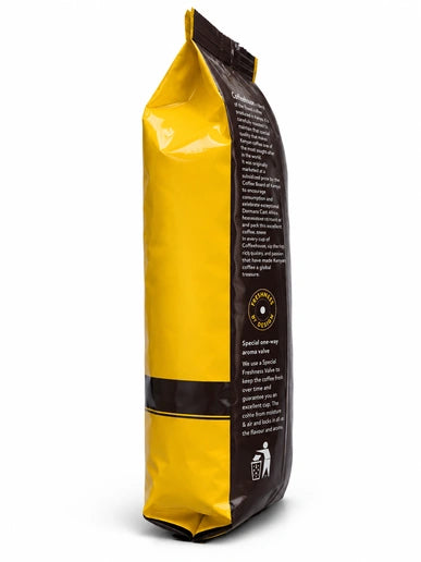 Dormans Coffeehouse Kenyan coffee 500g pouch shown in a close side view, featuring glossy yellow and brown packaging, Dormans Coffee Experts branding, dark brown side information panel, sealed coffee pouch construction, freshness valve information, quality roasting emblem and medium roast Kenyan coffee packaging, presented with realistic three-dimensional depth, studio lighting, subtle highlights and natural shadow on a clean white background.