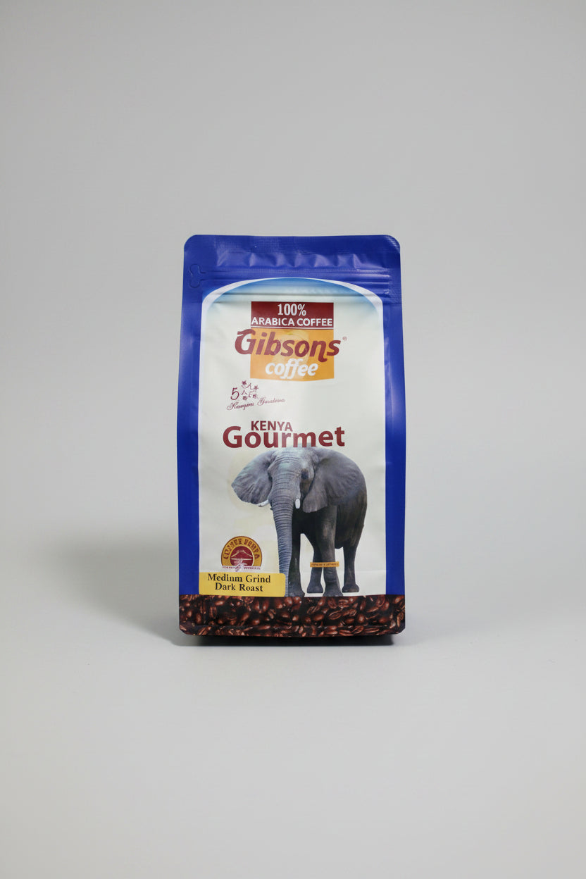 A bag of Gibson's Coffee Kenya Gourmet medium grind dark roast coffee, featuring a blue and white package with an elephant graphic, set against a dark fabric background. Gibsons Kenya Gourmet Coffee 400g dark roast medium grind, premium Kenyan ground coffee with a bold roast profile and convenient ready to brew format.