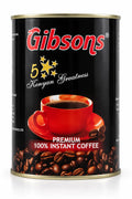 Gibsons Premium 100% Instant Coffee tin displayed in a polished studio view with black packaging, red cup, Kenyan Greatness emblem, roasted coffee beans, and bold branding for US shoppers seeking authentic Kenyan instant coffee and convenient everyday brewing at home.